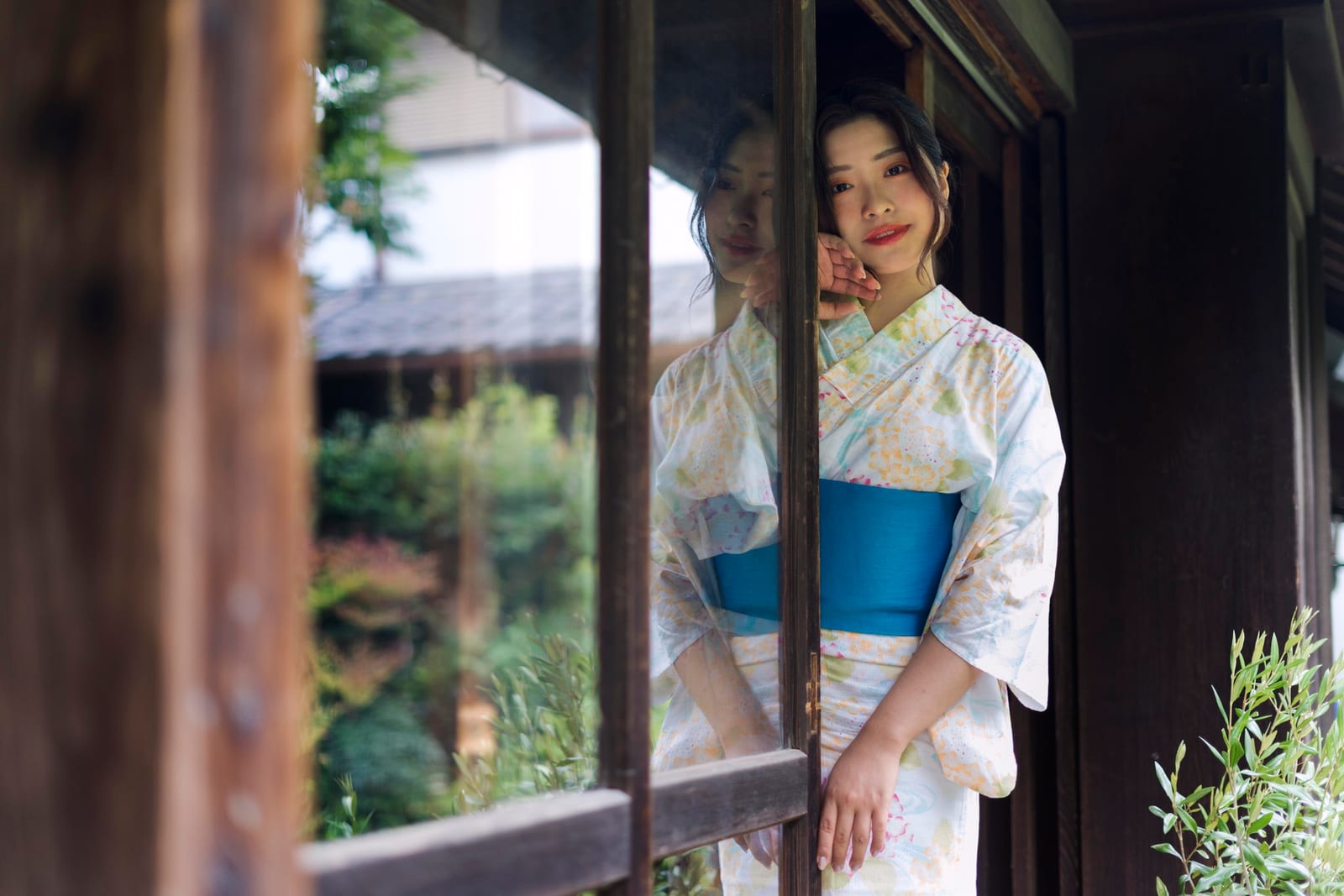 浴衣姿の女性が伝統的な日本家屋の木戸のそばに立つ様子